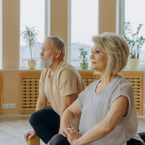 A diverse group of people practicing a basic yoga pose together in a bright room.